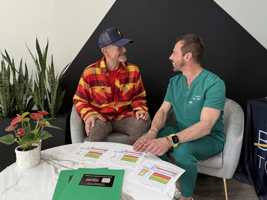 Two men conversing while reviewing bone density reports at a modern table with potted plant and printed charts.