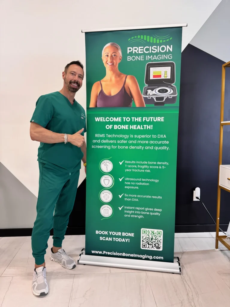Man in teal scrubs standing next to a Precision Bone Imaging banner in a clinic.