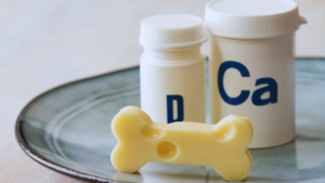 Bone-shaped cheese with calcium and vitamin D supplement bottles on plate, representing essential nutrients for bone health and osteoporosis prevention.