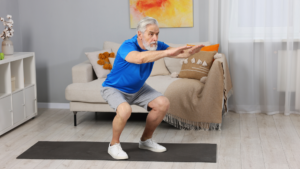 Senior man performing squat exercise at home on fitness mat in living room.